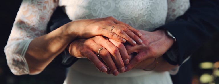 Braut und Bräutigam halten ihre Hände in edler Pose vor dem Bauch